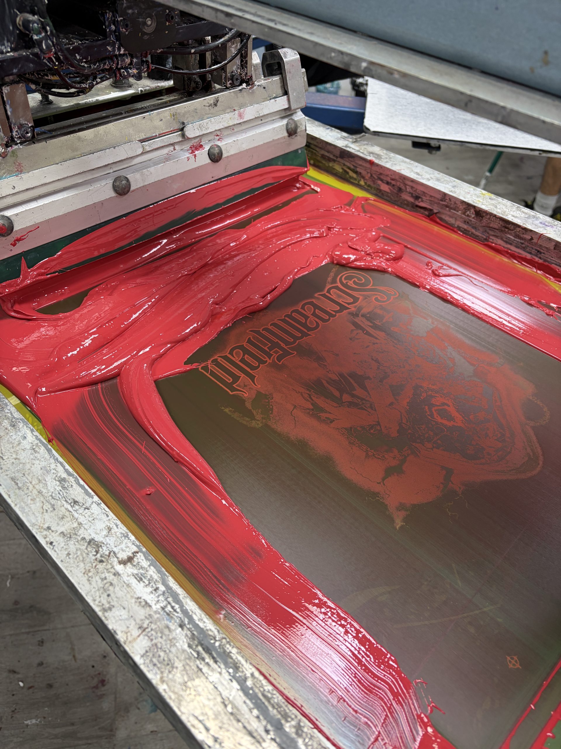 Pantalla de serigrafía con tinta roja y rasqueta durante la impresión en el taller de MarcaTuLogo