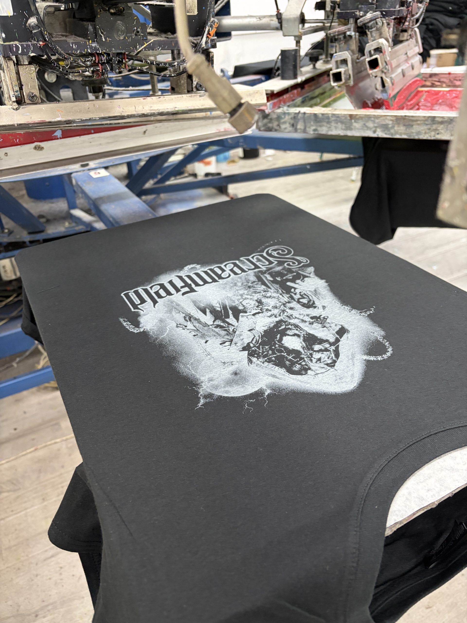 Detalle de un diseño blanco serigrafiado sobre una camiseta negra en el taller de MarcaTuLogo